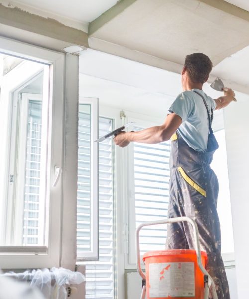 45298202 - thirty years old manual worker with wall plastering tools inside a house. plasterer renovating indoor walls and ceilings with float and plaster.